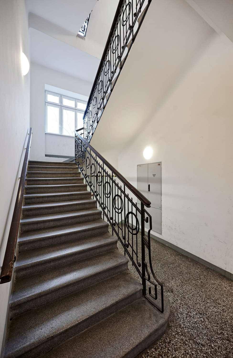 Helles Treppenhaus mit klassischem schmiedeeisernem Geländer und Fenster für natürliches Licht.
