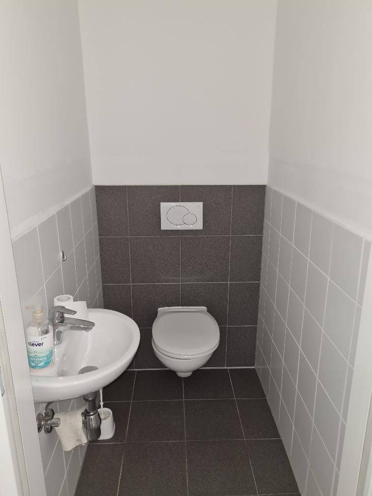 Gäste-WC mit Wand-WC, kleinem Waschbecken und modernen Fliesen.