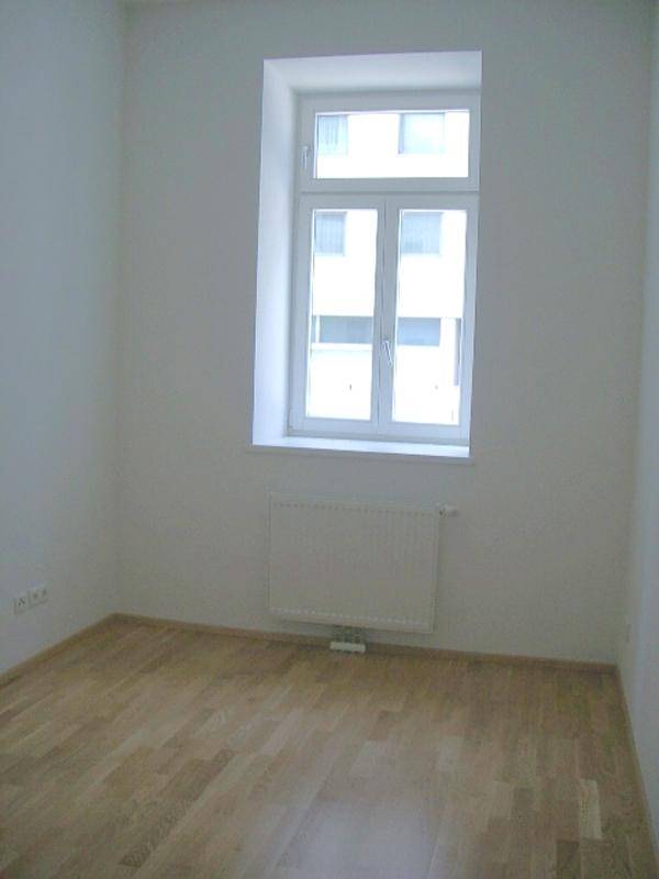 Heller, leerer Raum mit Parkettboden, Fenster und Heizkörper, bereit zur individuellen Gestaltung.