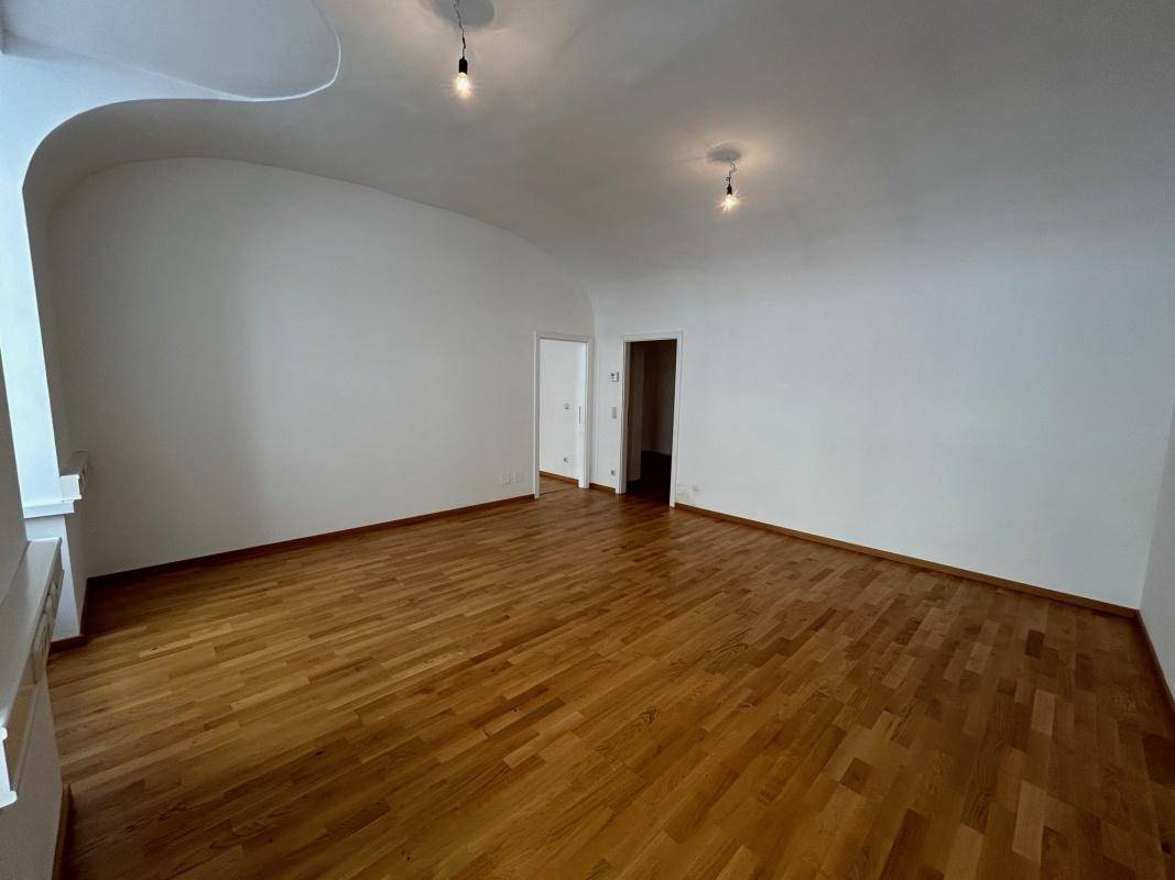Geräumiges Wohnzimmer mit Parkettboden und schlichter weißer Wandgestaltung.
