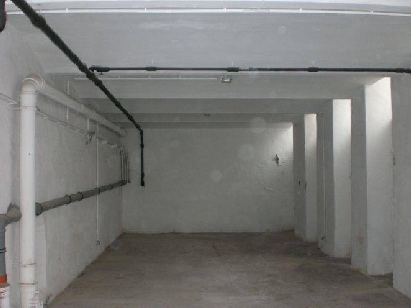 Ein großer, leerer Kellerraum mit Betonboden, Säulen und sichtbaren Rohren an der Decke.