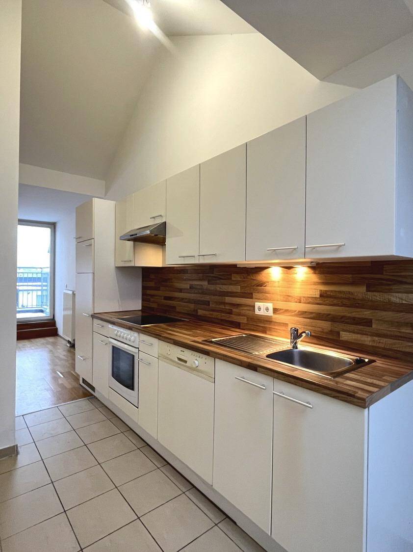Einbauküche mit weißen Fronten, Holz-Arbeitsplatte und Fliesenboden, gut beleuchtet.