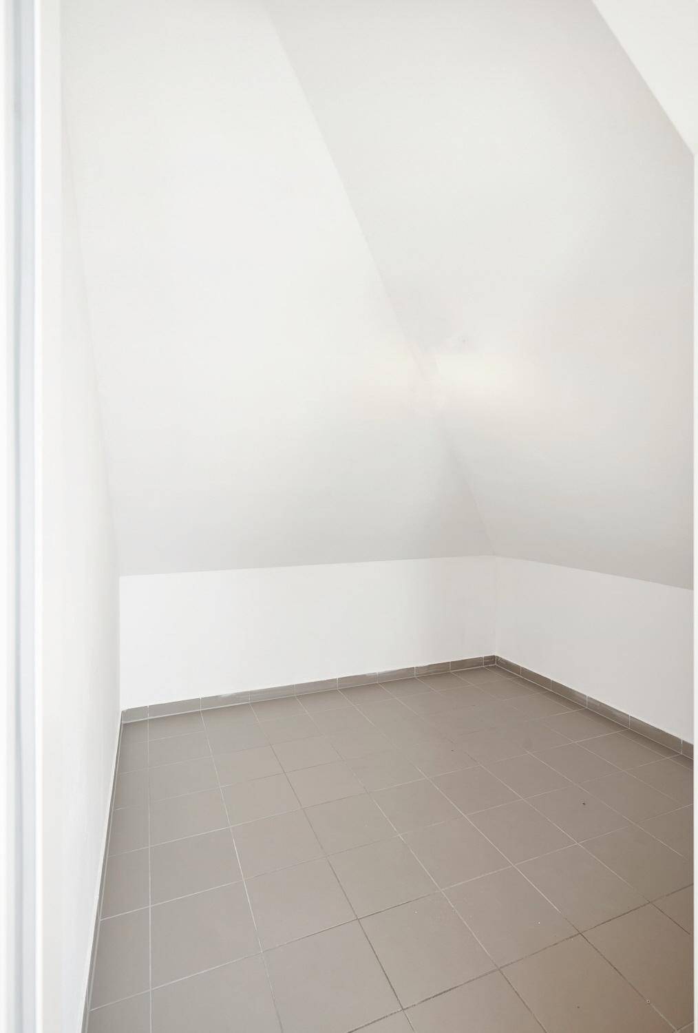 Kleiner Abstellraum mit Fliesenboden und schrägen Wänden im Dachgeschoss.