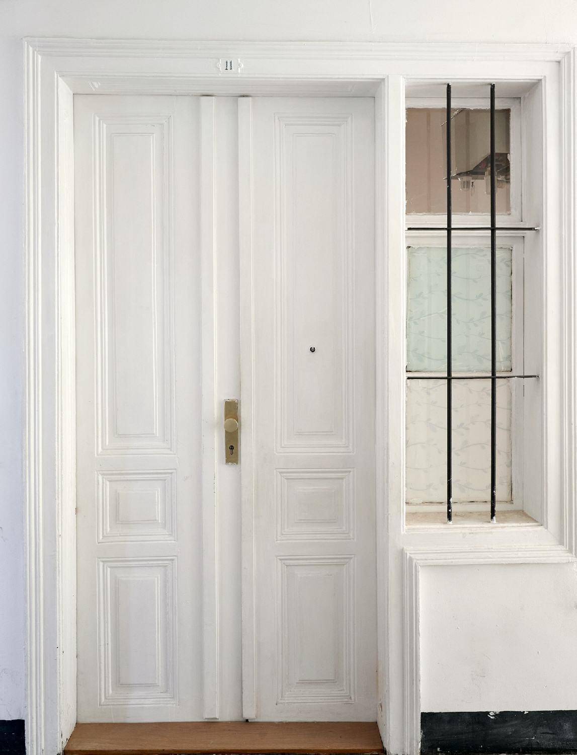 Weiße Eingangstür mit dekorativen Paneelen und einem vergitterten Seitenfenster, klassischer Stil.