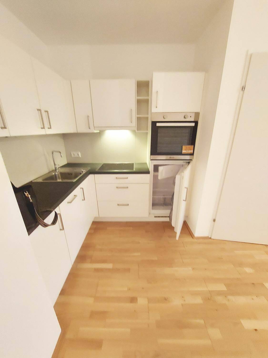 Moderne Küchenzeile mit weißen Schränken, integriertem Backofen und Kühlschrank.