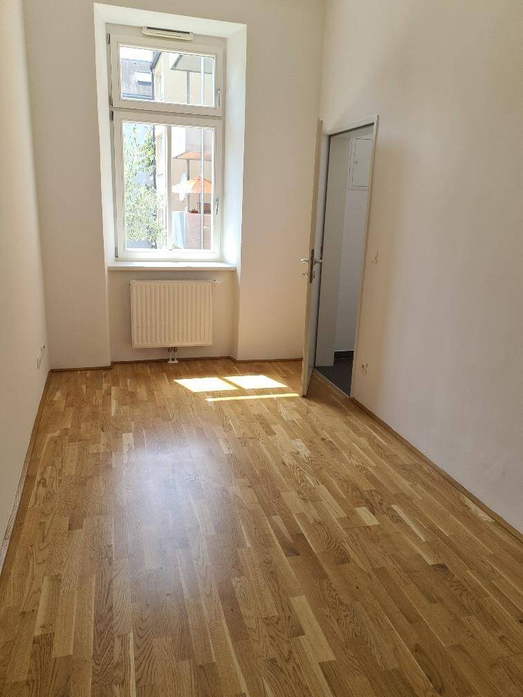 Kleiner, heller Raum mit Holzboden und einem Fenster, ideal als Schlaf- oder Arbeitszimmer.