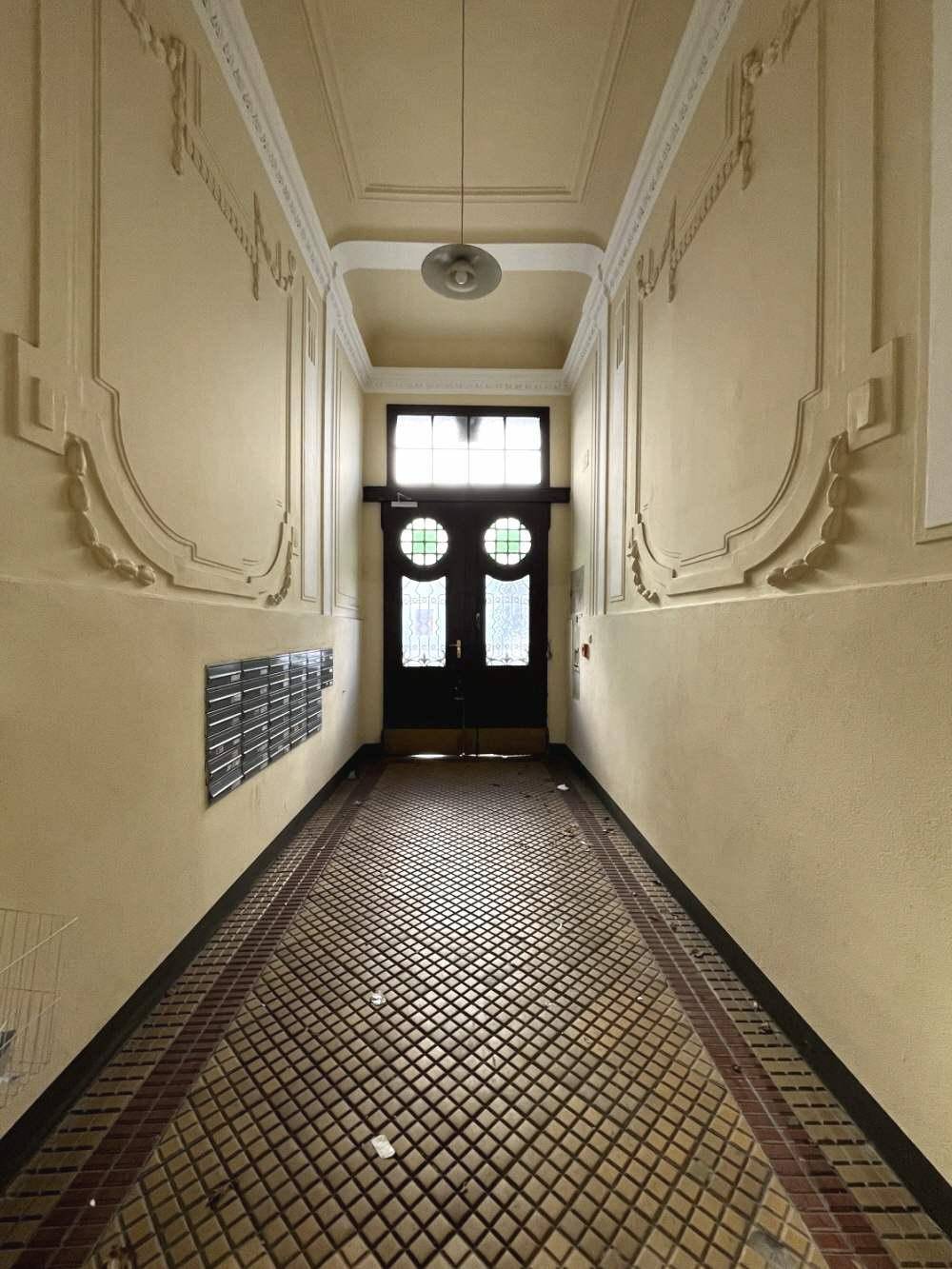 Langer Eingangsbereich mit Stuckverzierungen an der Decke, Fliesenboden und Briefkästen.