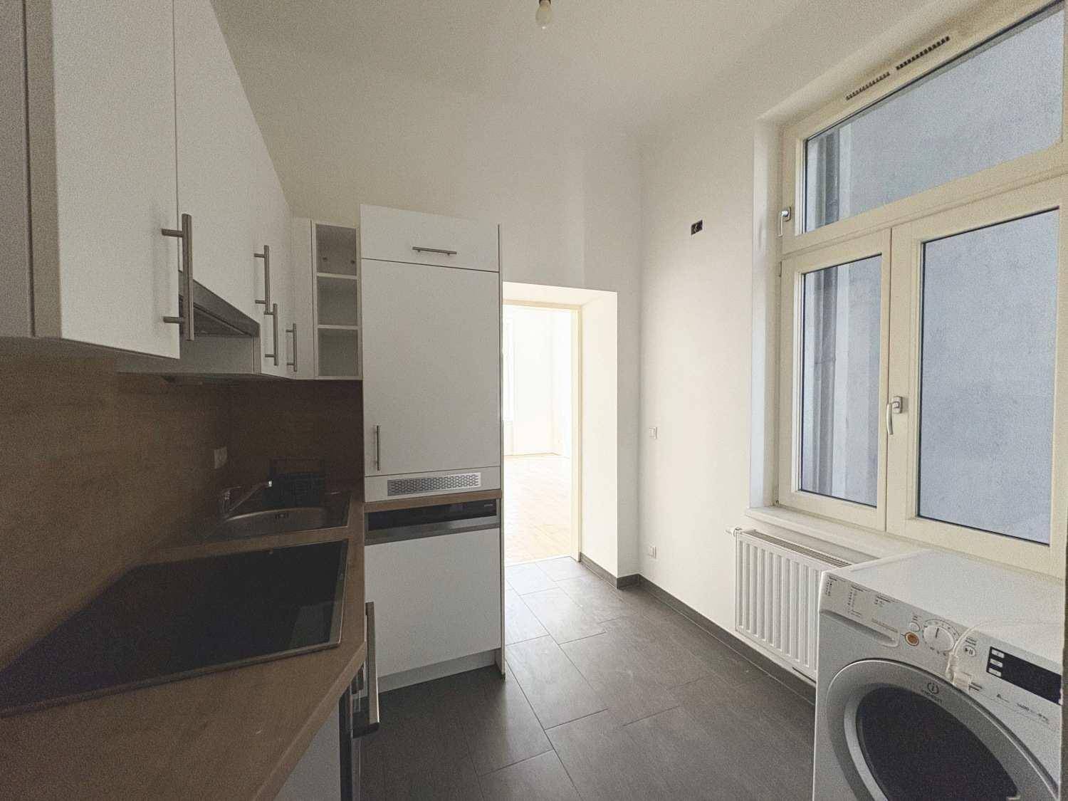 Kleine Küche mit weißen Schränken, integriertem Kühlschrank und Waschmaschine unter dem Fenster.