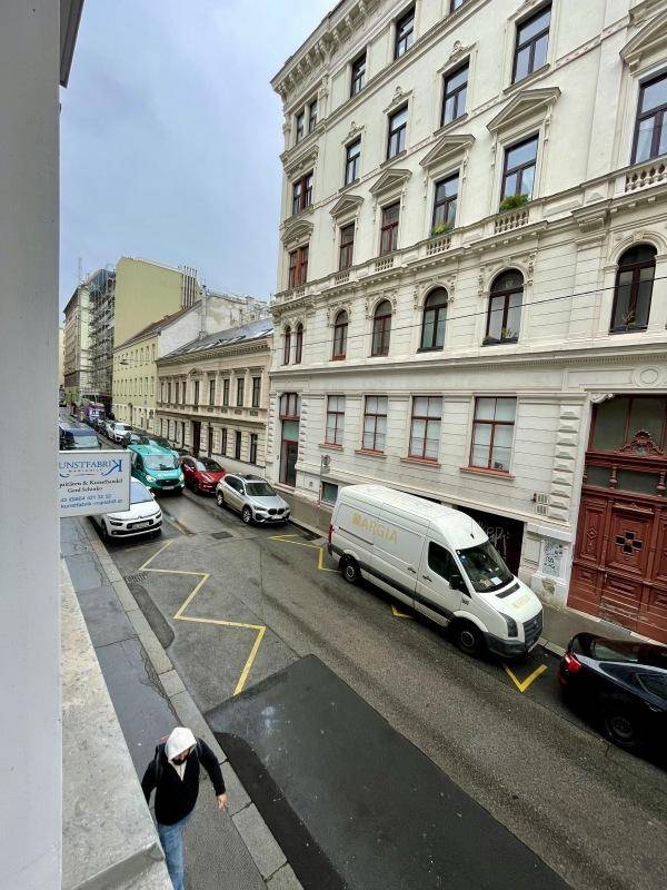 Blick von oben auf eine belebte Stadtstraße mit parkenden Autos und historischen Gebäuden.