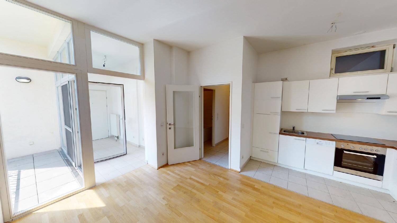Offener Wohnbereich mit integrierter Küche, Parkettboden und Zugang zum Balkon.