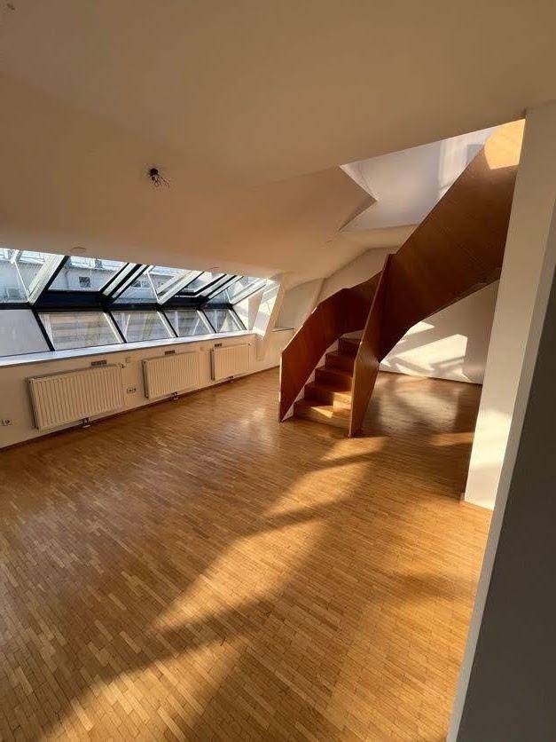 Lichtdurchfluteter Dachgeschossraum mit Holzparkettboden, großen Fenstern und einer modernen Holztreppe.