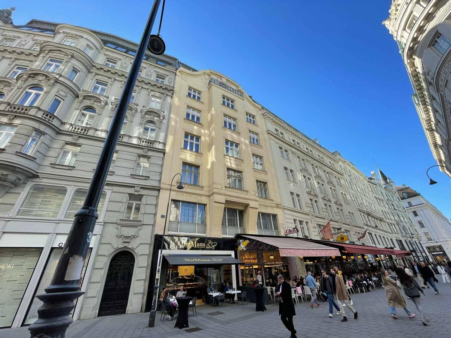 Lebhafte Straße mit historischen Gebäuden, Geschäften und Cafés, belebt von Passanten unter blauem Himmel.