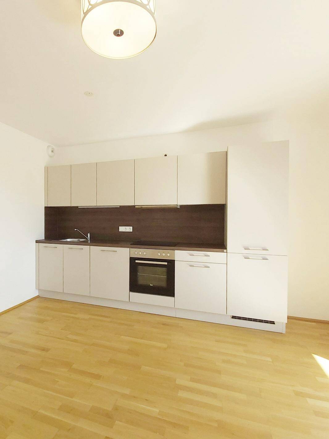 Moderne Küchenzeile mit hellen Schränken, dunkler Arbeitsplatte und integriertem Backofen.