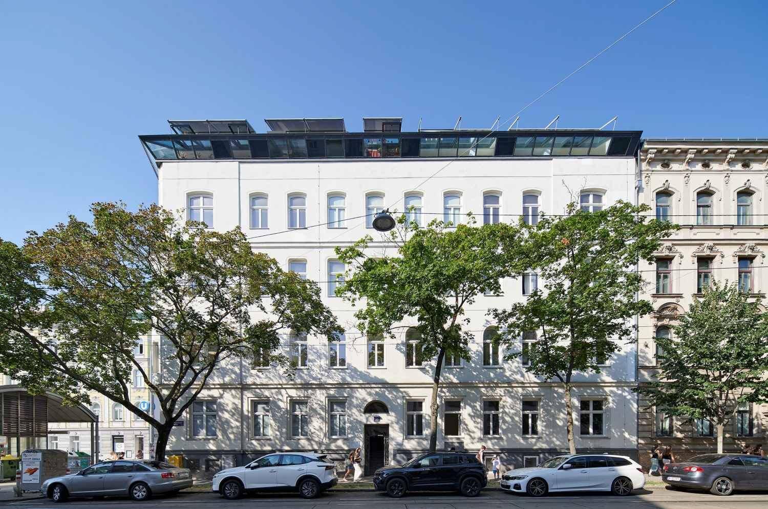 Moderne Fassade eines Wohngebäudes mit Dachaufbau und parkenden Autos davor.
