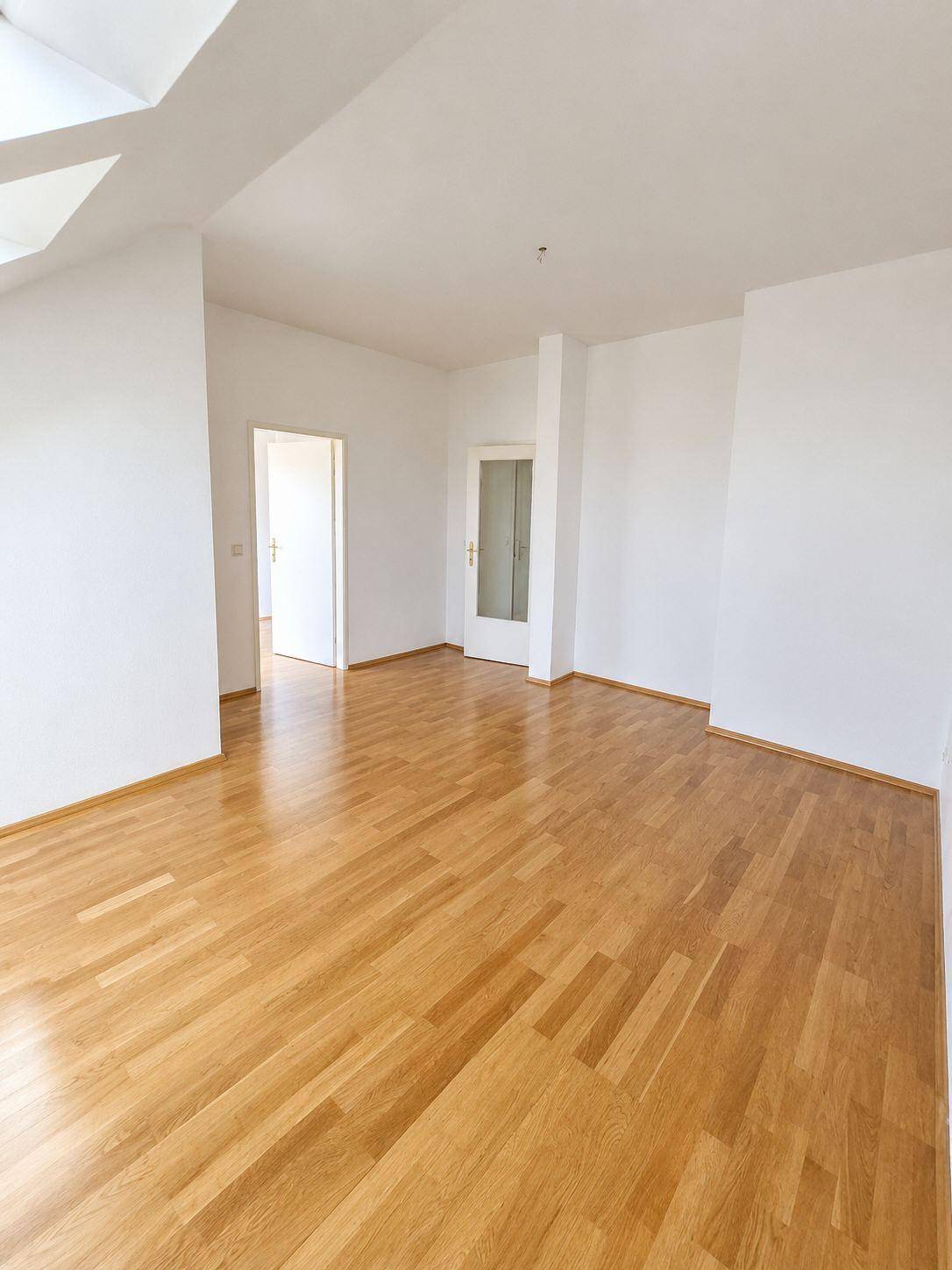 Geräumiger Wohnbereich mit hellem Holzfußboden und Zugang zu weiteren Zimmern.