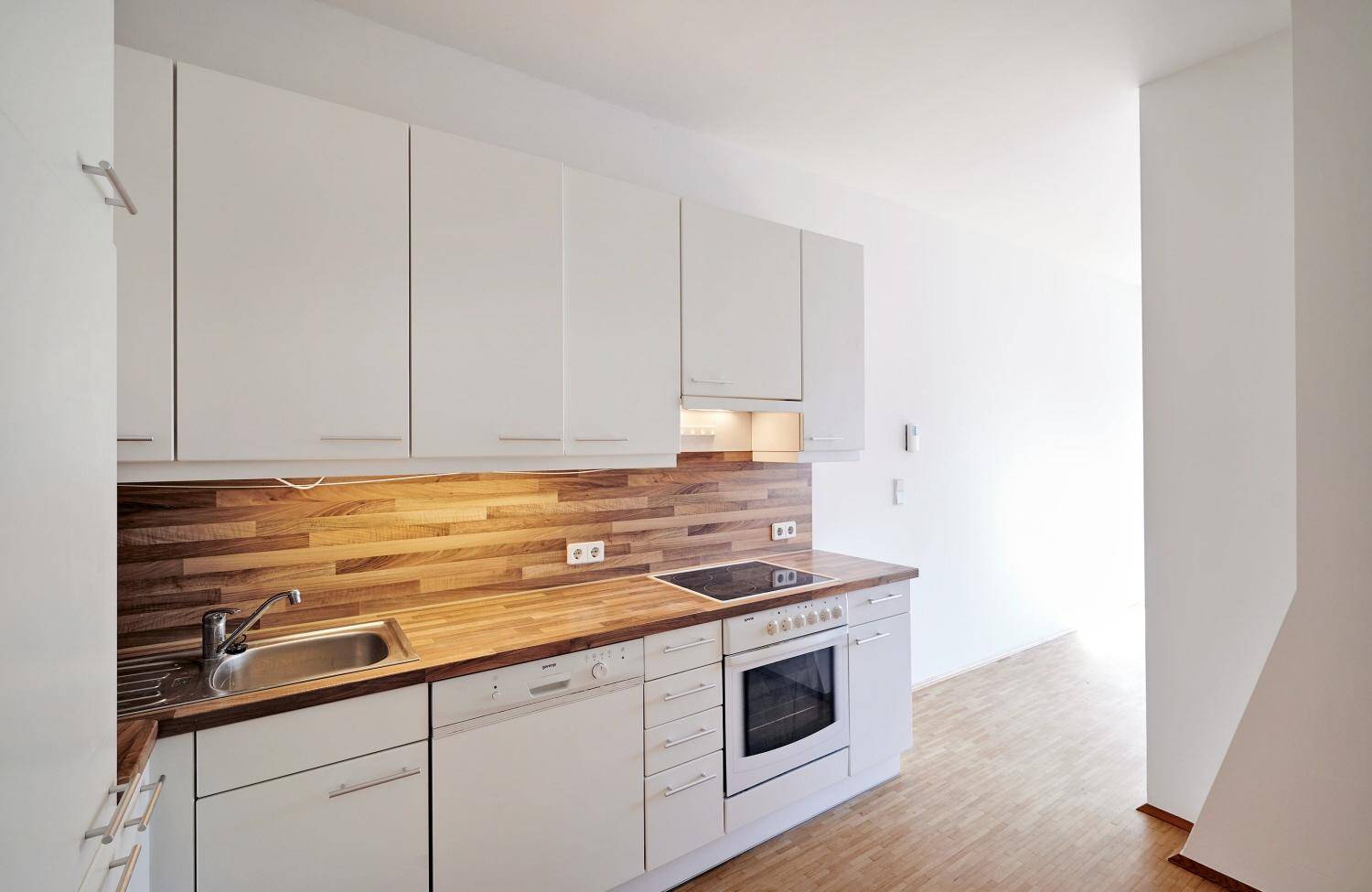 Moderne Einbauküche mit weißen Schränken, Holzarbeitsplatte und integrierten Geräten.