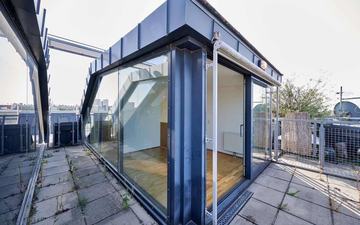 Dachterrasse mit Zugang zum hellen Innenraum durch große Glasschiebetüren und Stadtblick.