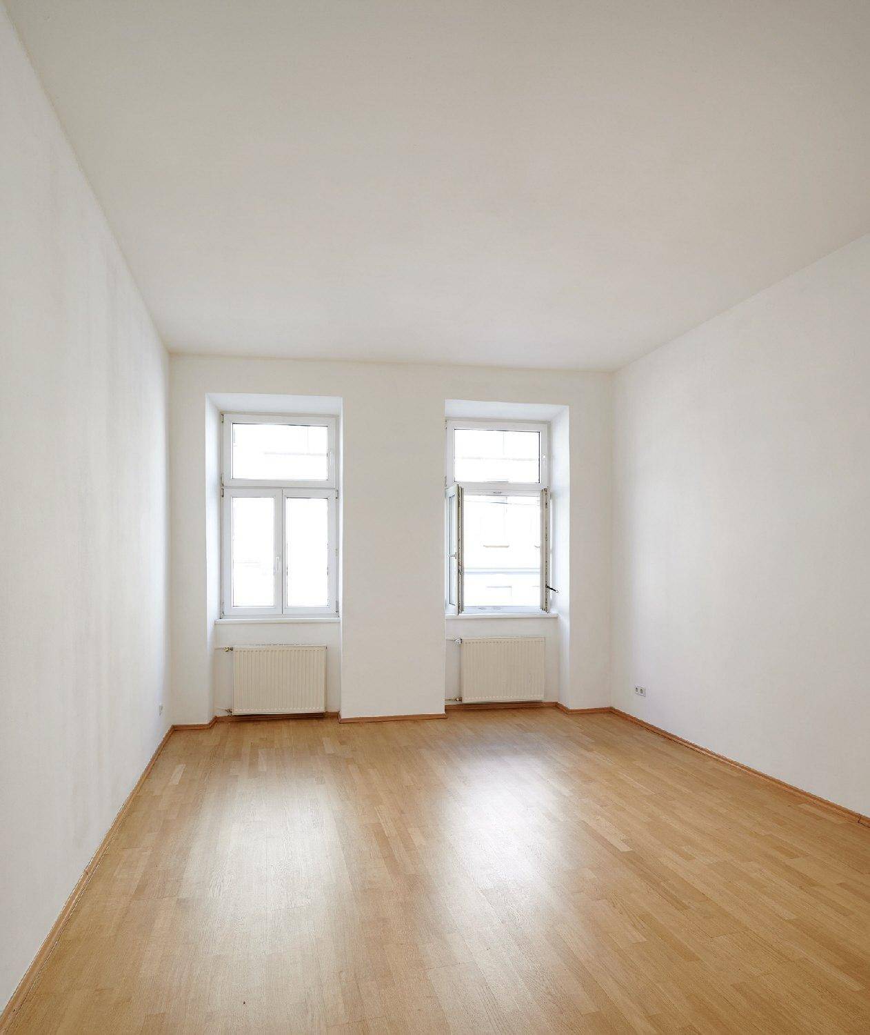 Heller, leerer Raum mit Parkettboden und zwei großen Fenstern, ideal für individuelle Einrichtung.