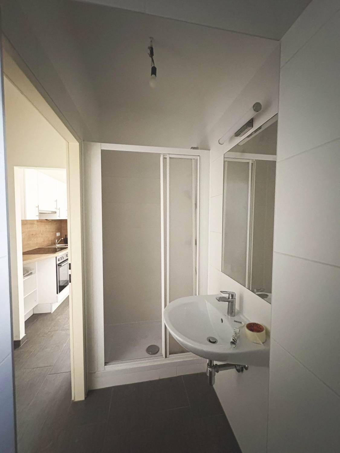 Modernes Badezimmer mit Duschkabine, Waschbecken und Blick in die angrenzende Küche.