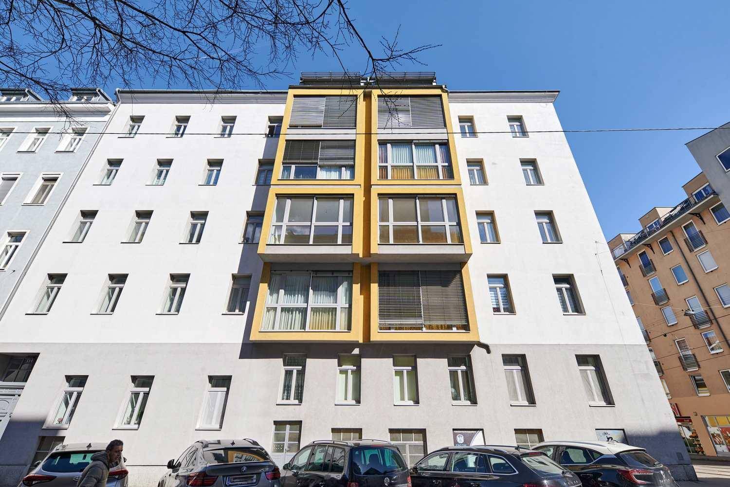 Frontansicht des Gebäudes mit markanten gelben Balkonstrukturen und zahlreichen Fenstern.