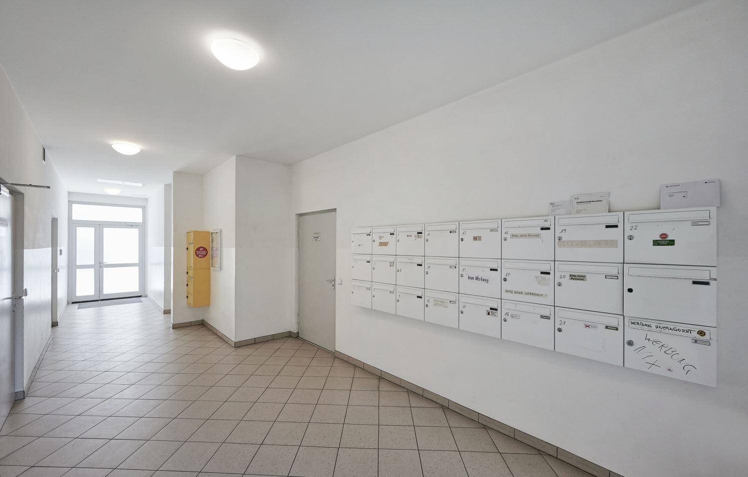 Gemeinschaftlicher Flurbereich mit Briefkästen und Fliesenboden, der zum Ausgang des Gebäudes führt.