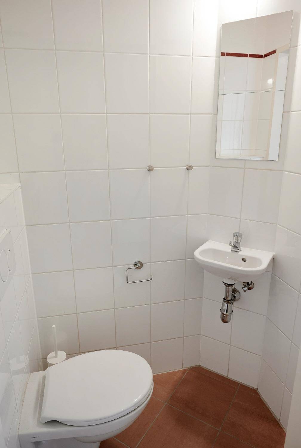 Kleines Gäste-WC mit weißen Fliesen, Waschbecken und Toilette, funktional eingerichtet.
