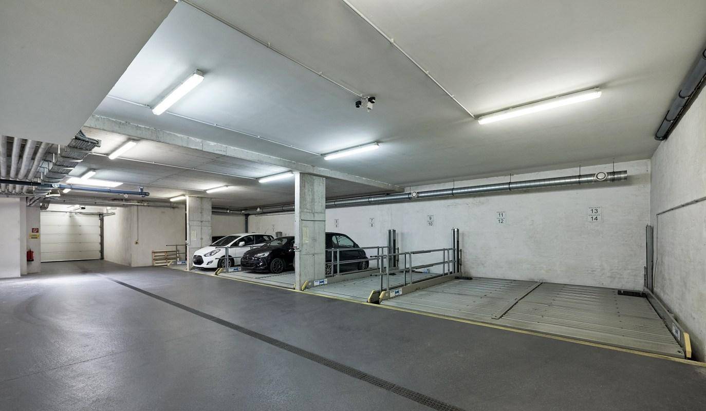 Geräumige Tiefgarage mit mehreren Autohebebühnen und einer Zufahrt im Hintergrund.
