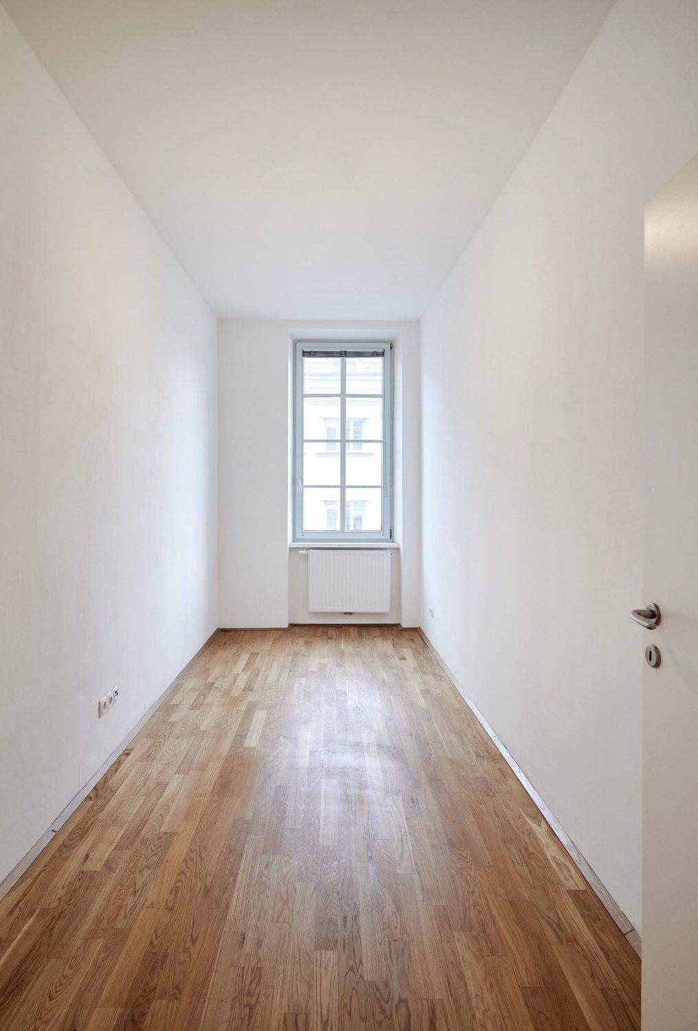 Langes, schmales Zimmer mit Parkettboden und einem Fenster, ideal als Schlaf- oder Arbeitszimmer.
