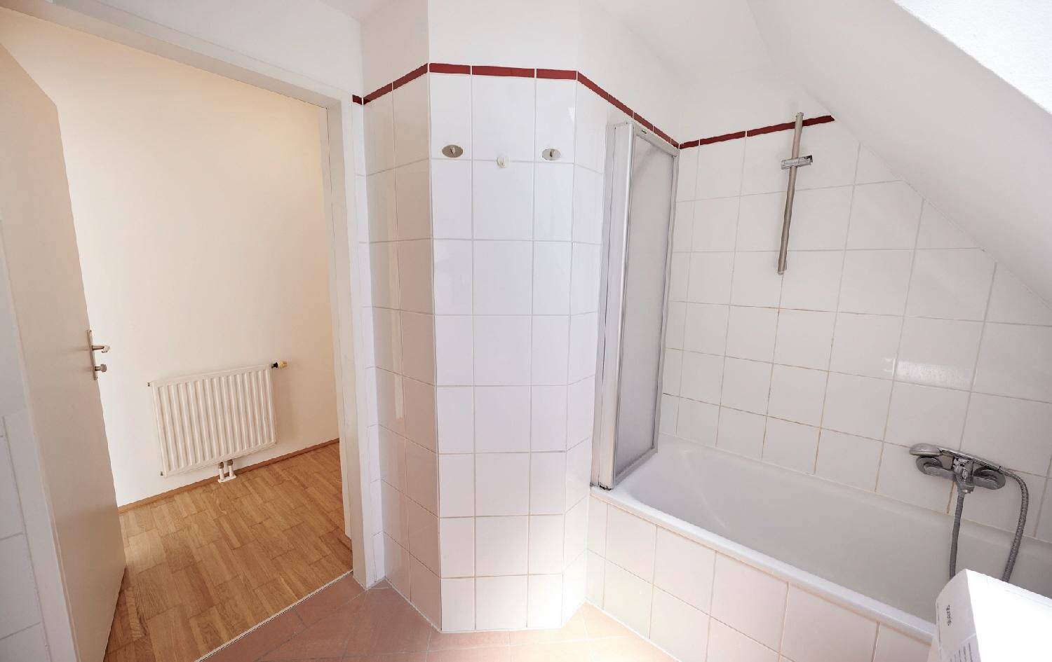 Badezimmer im Dachgeschoss mit Badewanne, Duschabtrennung und weißen Fliesen.