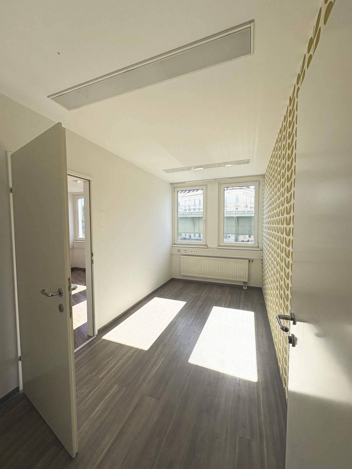 Kleinerer Raum mit Holzboden, Fenstern und einer Wand mit auffälligem Muster.