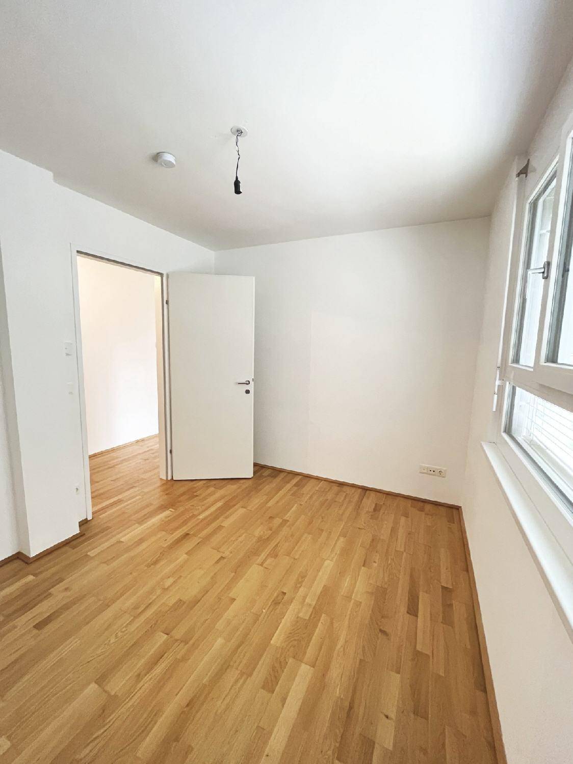 Geräumiges Schlafzimmer mit Parkettboden und einem Fenster, das viel Licht hereinlässt.