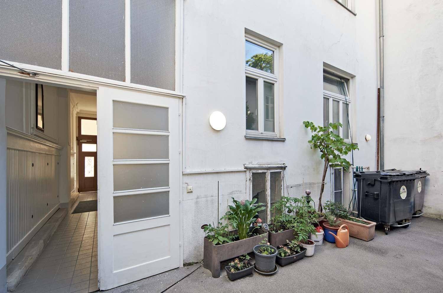 Ein kleiner Innenhof mit Pflanzenkübeln, Mülltonnen und einem Ausgang zum Gebäudeinneren.