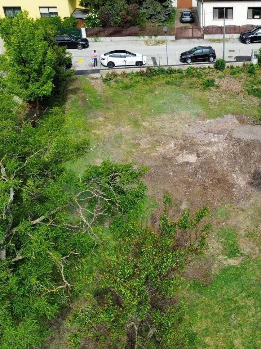 Luftaufnahme des Grundstücks mit Blick auf die angrenzende Straße und parkende Fahrzeuge unter grünen Bäumen.