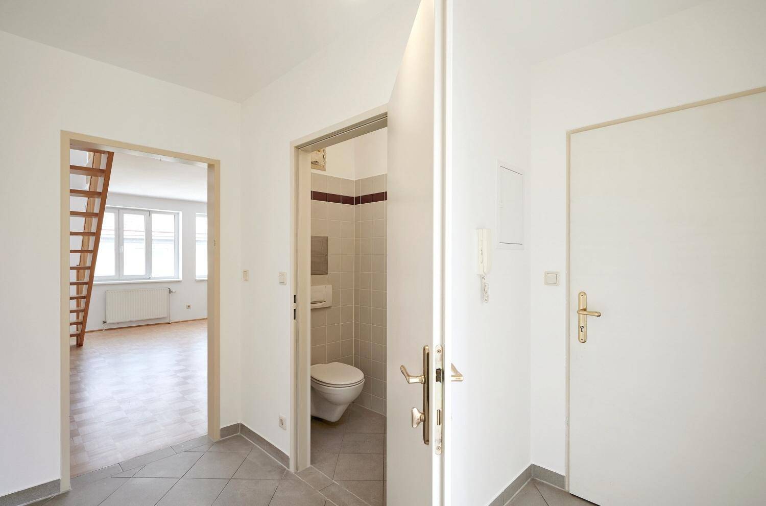 Heller Flur mit grauen Fliesen und Zugang zu einem Gäste-WC sowie dem Wohnbereich.