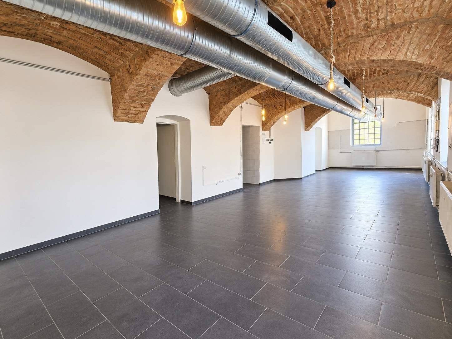 Weitläufiger Innenraum mit charakteristischer Gewölbedecke, Lüftungsrohren und dunklem Fliesenboden.