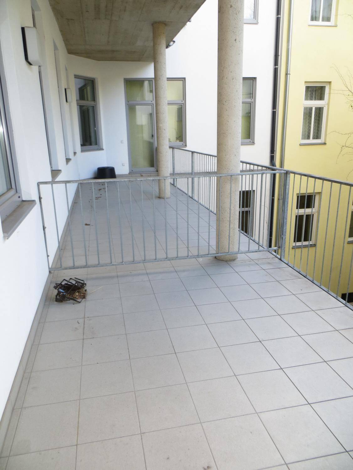 Langer, gefliester Balkon mit Metallgeländer und Säulen, bietet einen Blick in den Innenhof.