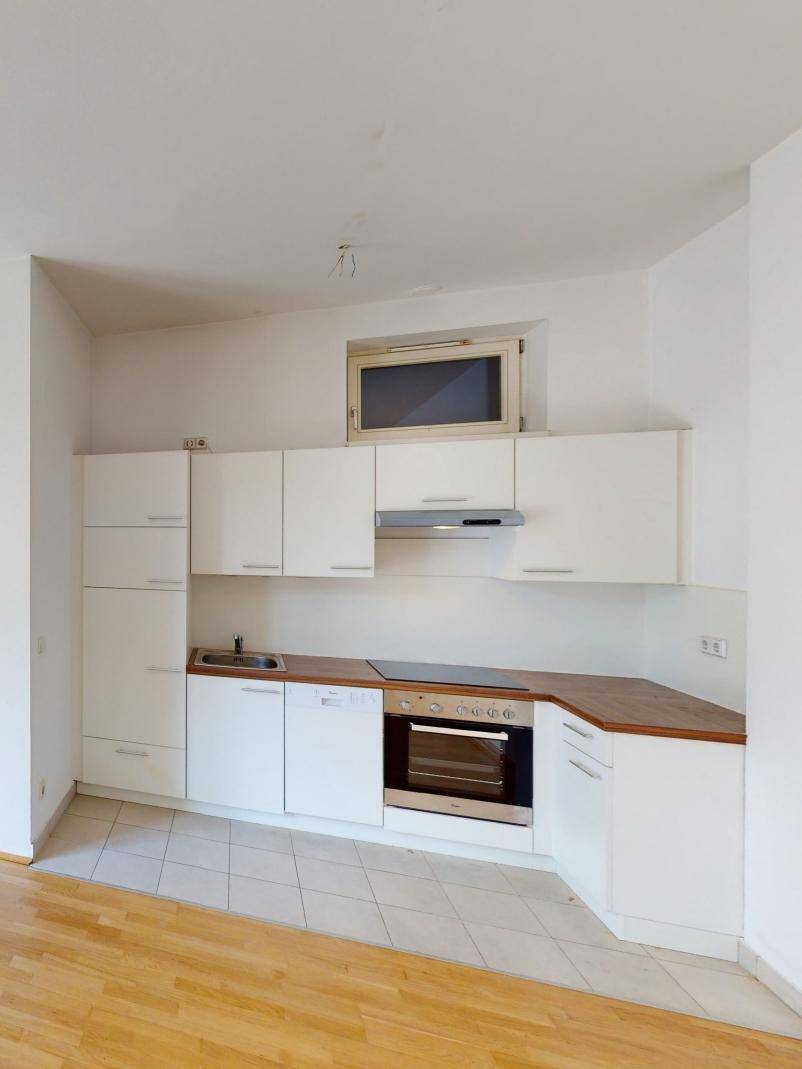 Funktionale Einbauküche mit weißen Schränken, Holz-Arbeitsplatte und integrierten Geräten.