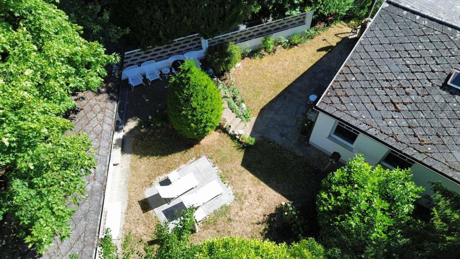 Gartenbereich mit gepflasterten Sitzgelegenheiten und Rasenflächen, umgeben von Bäumen.
