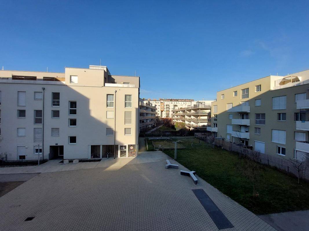 Außenansicht moderner Wohngebäude mit begrüntem Innenhof und sonnigen Freiflächen.