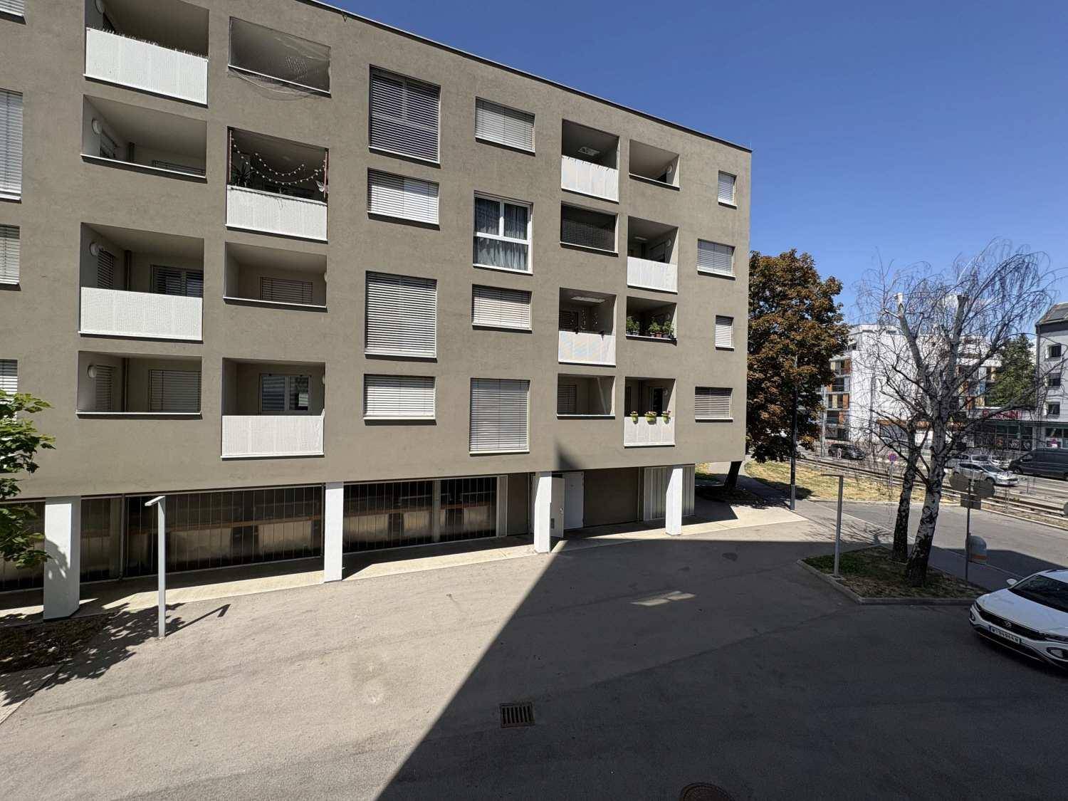 Moderne Gebäudefassade mit Balkonen und Außenparkplätzen unter blauem Himmel.