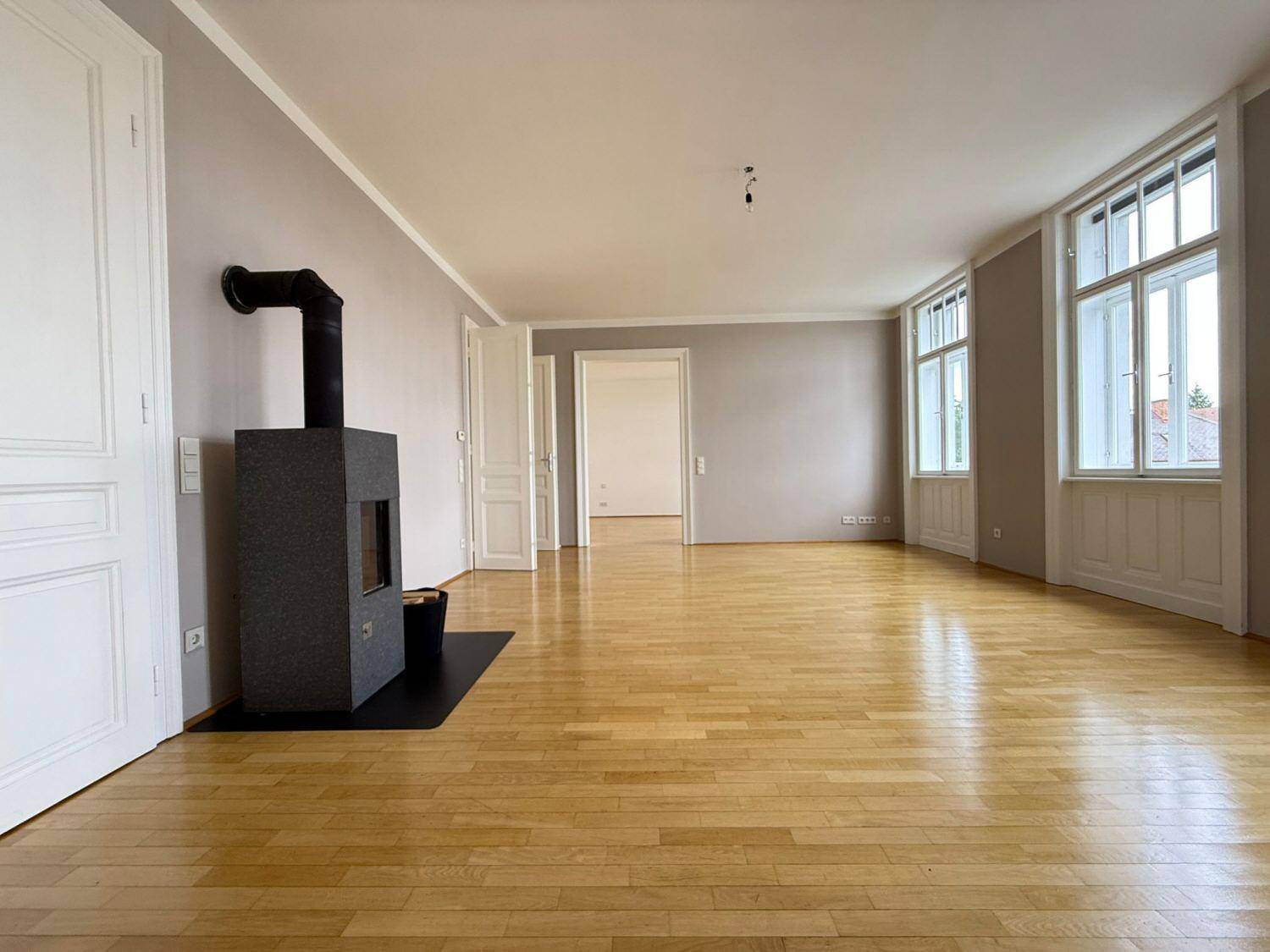 Helles Wohnzimmer mit Parkettboden, modernem Kaminofen und hohen Fenstern.