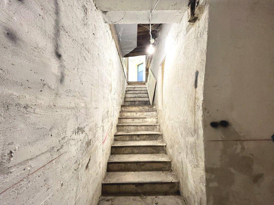 Steile Kellertreppe mit rauen Betonstufen und einfacher Beleuchtung, die nach oben führt.