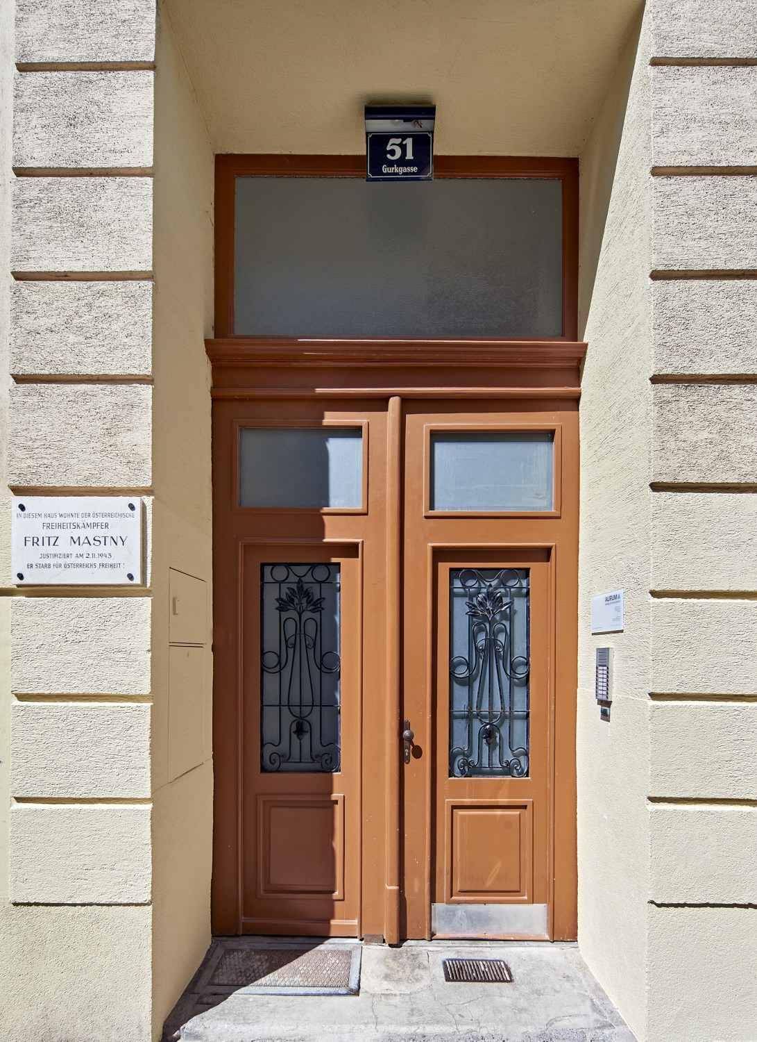 Ein historischer Hauseingang mit Holztüren, Glasfenstern und einer Hausnummer über dem Portal.