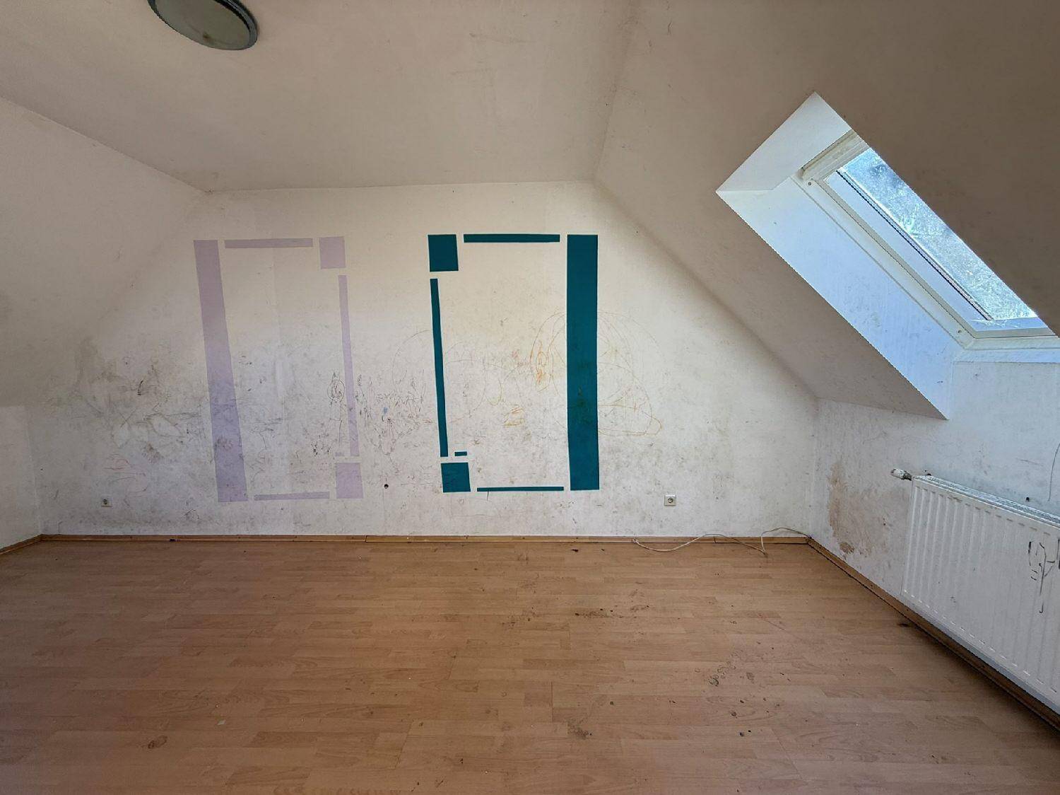 Dachgeschosszimmer mit Dachfenster und schrägen Wänden, renovierungsbedürftig.