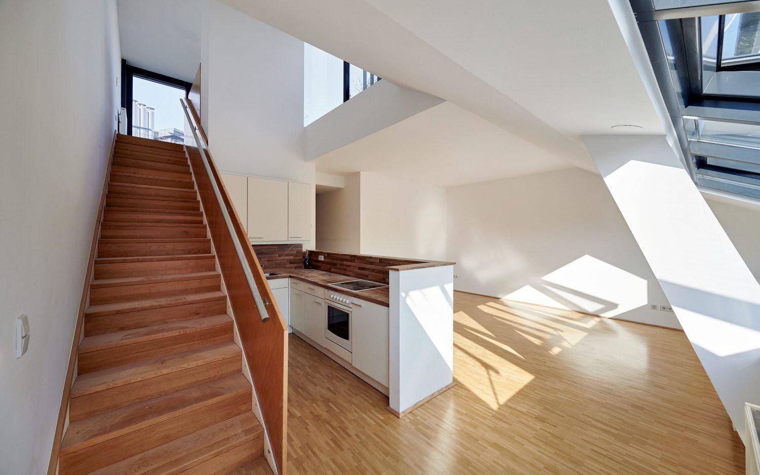 Offener Wohnbereich mit integrierter Küche, Holztreppe und viel Tageslicht.
