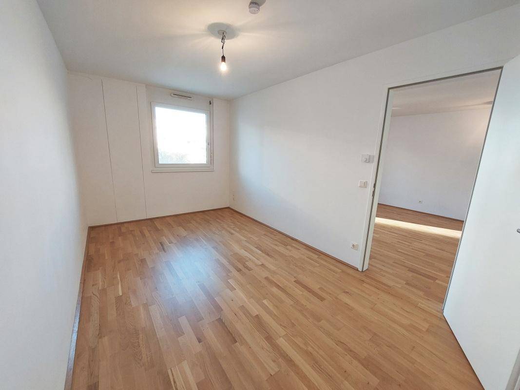 Helles Schlafzimmer mit Parkettboden und großem Fenster, bietet viel Tageslicht und eine ruhige Atmosphäre.