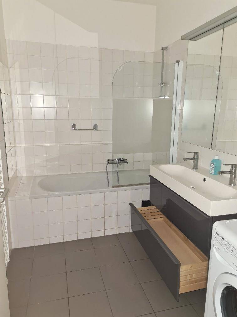 Badezimmer mit Badewanne, Duschwand, modernem Waschbecken, Spiegelschrank und Waschmaschine.