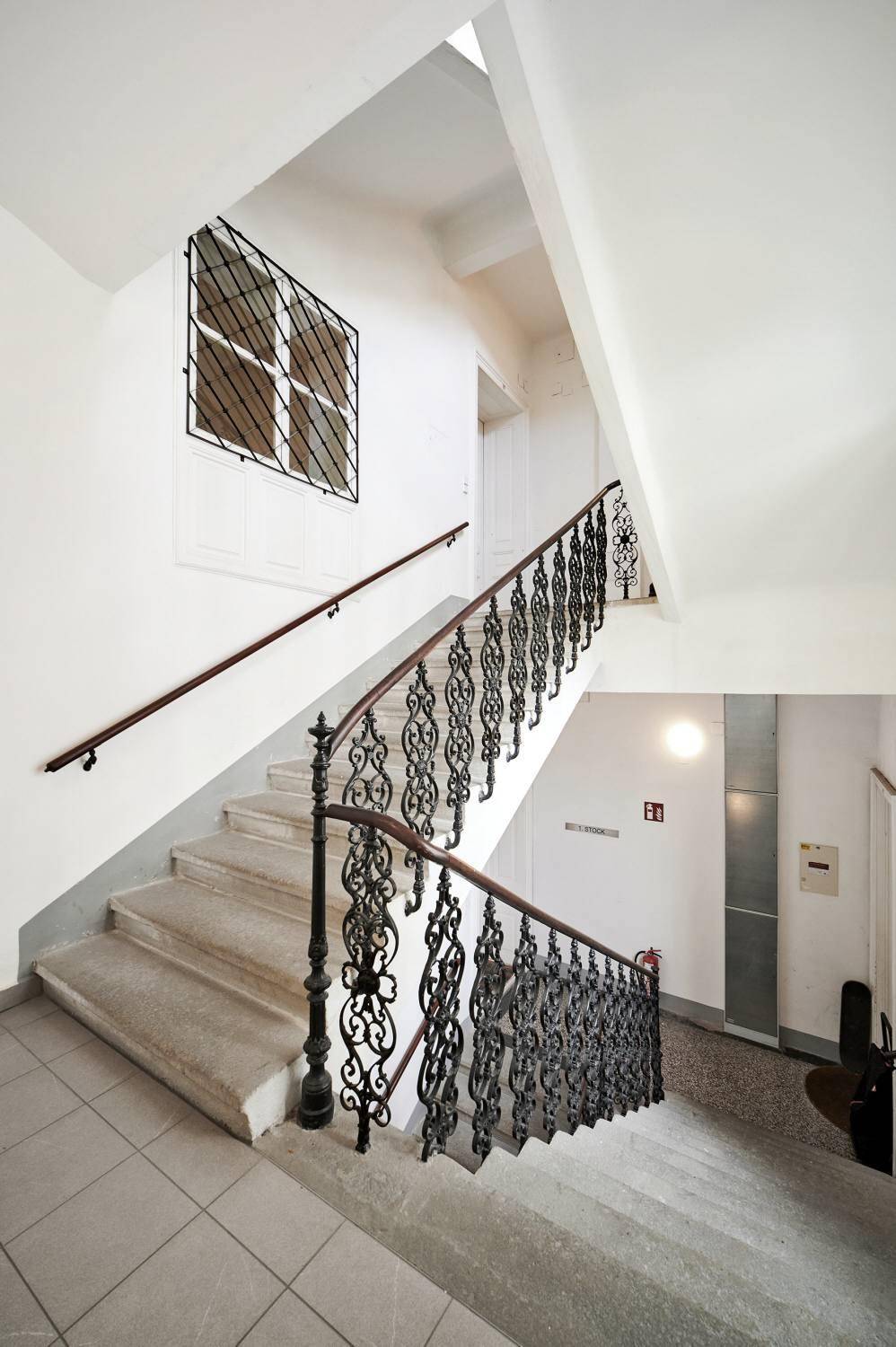 Historisches Treppenhaus mit schmiedeeisernem Geländer und Steinstufen in einem Altbau.