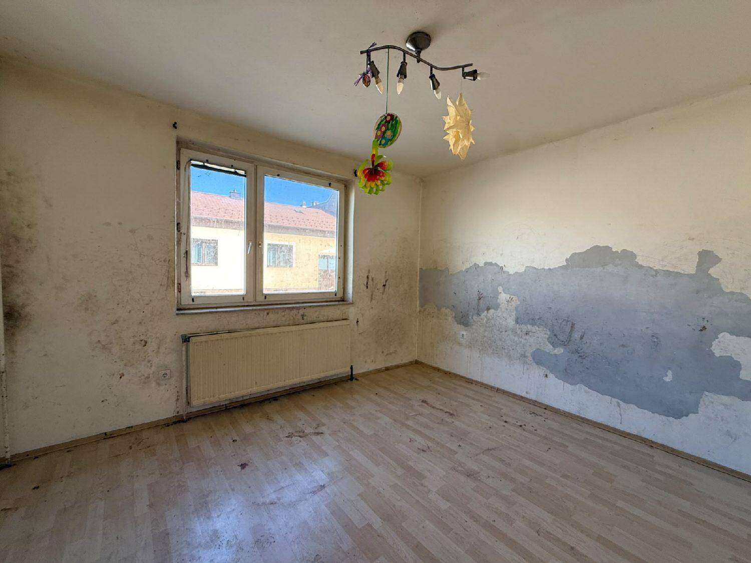 Helles Zimmer mit Fenster und Heizkörper, die Wände zeigen deutliche Gebrauchsspuren.