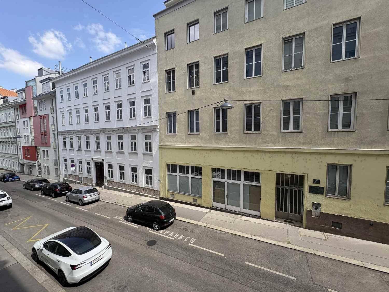 Blick auf eine belebte Stadtstraße mit parkenden Autos und historischen Gebäudefassaden.